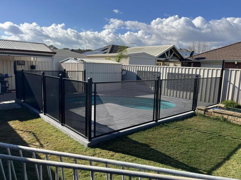 Black perforated aluminium pool fencing on a concrete footing around a backyard pool